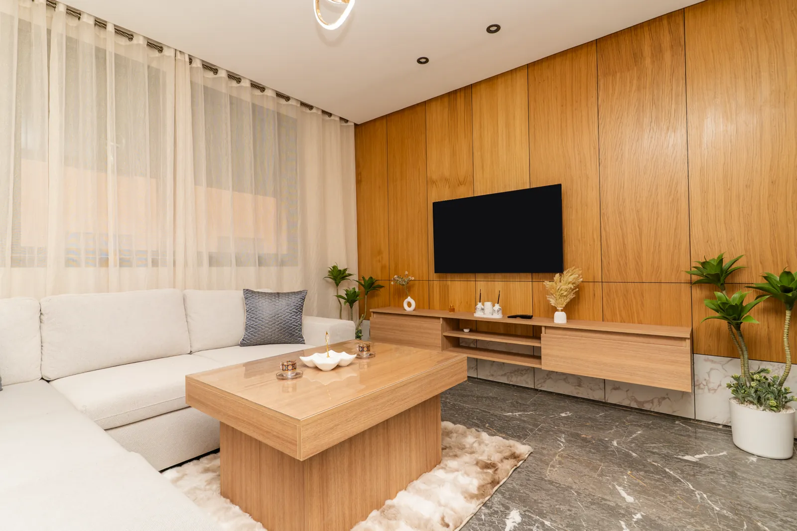 Salon d'un appartement meublé pour Airbnb à Marrakech : canapé d'angle, table basse en bois, télévision murale